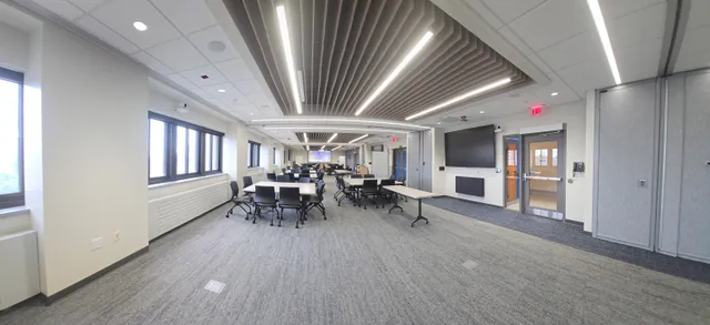 Another panoramic view of the same divisible conference room, showing the stepped seating platforms and folding chairs beneath the ceiling speakers. Close the doors and the screens reconfigure for each half.