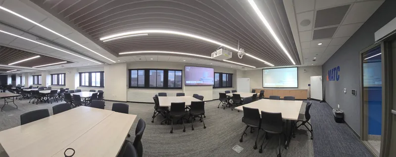 A wide panoramic view of a divisible conference room with stepped seating platforms and wall-mounted displays. Close the doors and the screens reconfigure. Eight cameras and 24 speakers serve the one room.