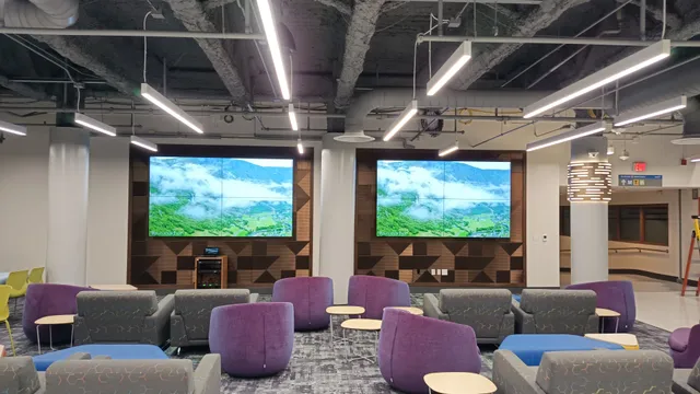 A student lounge with two four-panel video walls displaying scenic content, surrounded by purple and gray lounge seating.