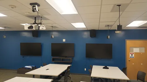 Three flat-panel displays fully mounted and wired on a blue accent wall, with the ceiling projector, camera, and speakers all in place.